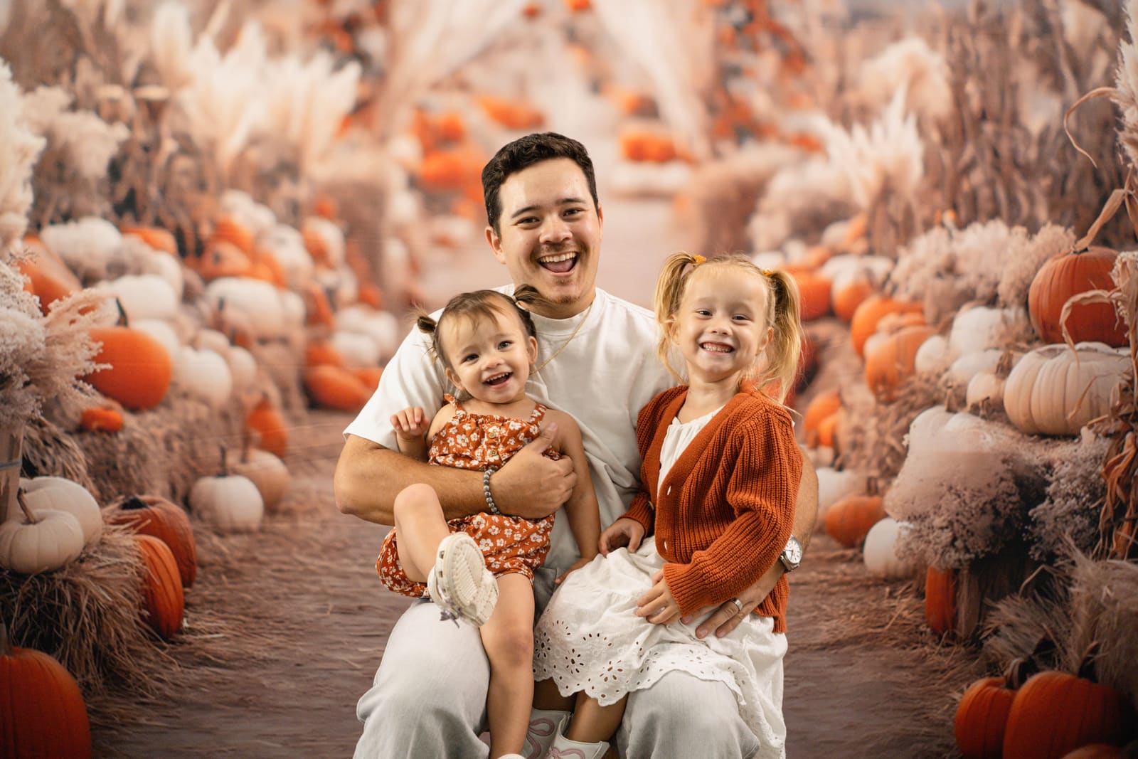 Father kneeling with his toddler and preschooler, all laughing, in the pumpkin patch mini set.