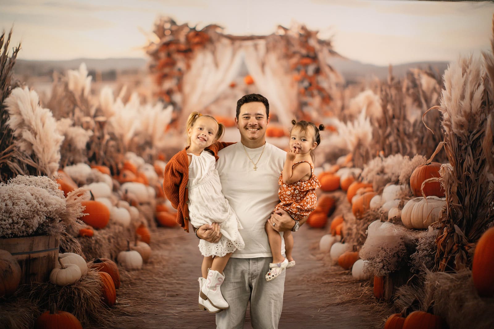 Father carrying both of his young daughters down the pumpkin patch path.