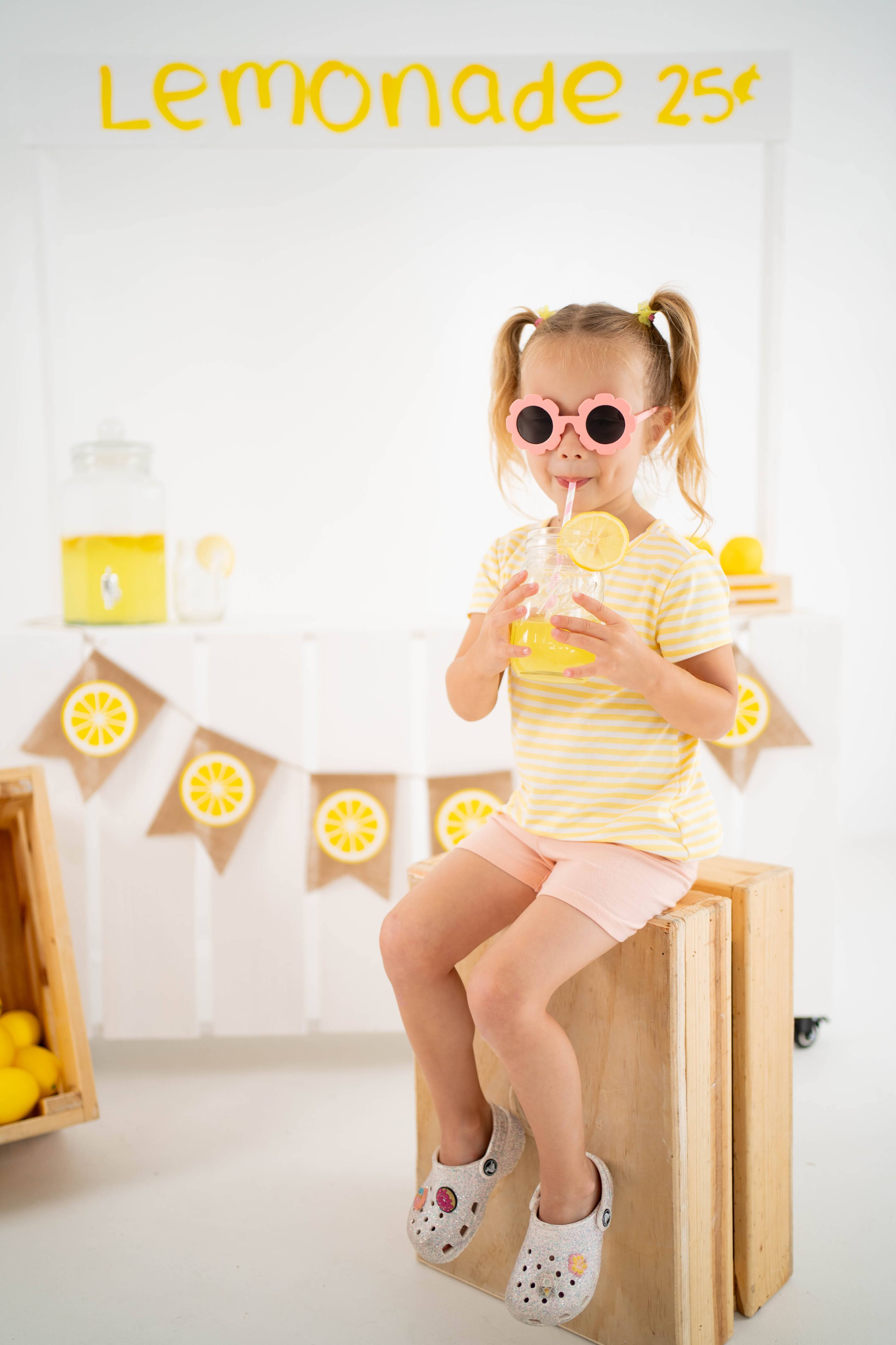 Girl laughing in pink sunglasses at the lemonade mini stand.