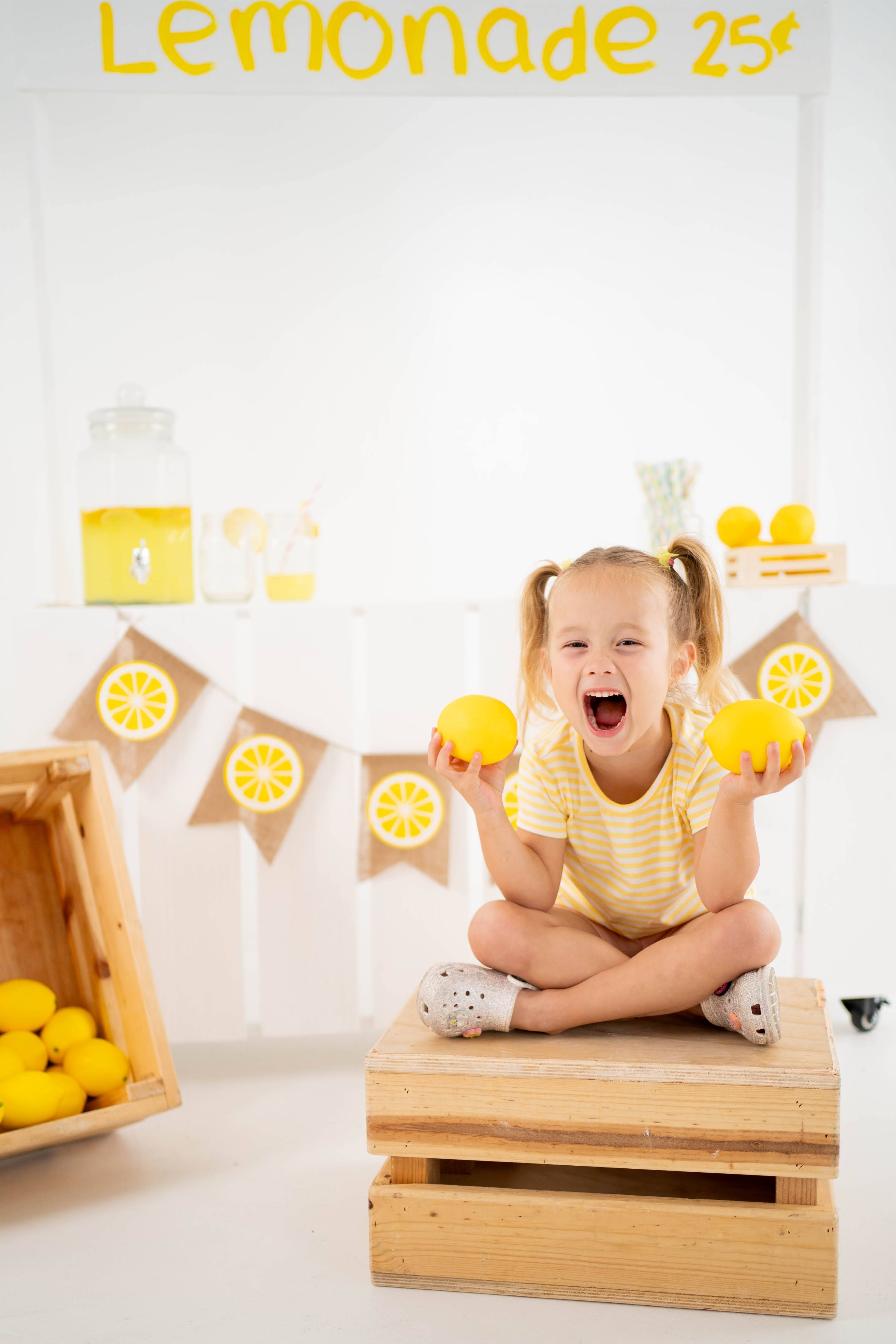 Girl laughing with lemons at a bright indoor lemonade stand mini session.