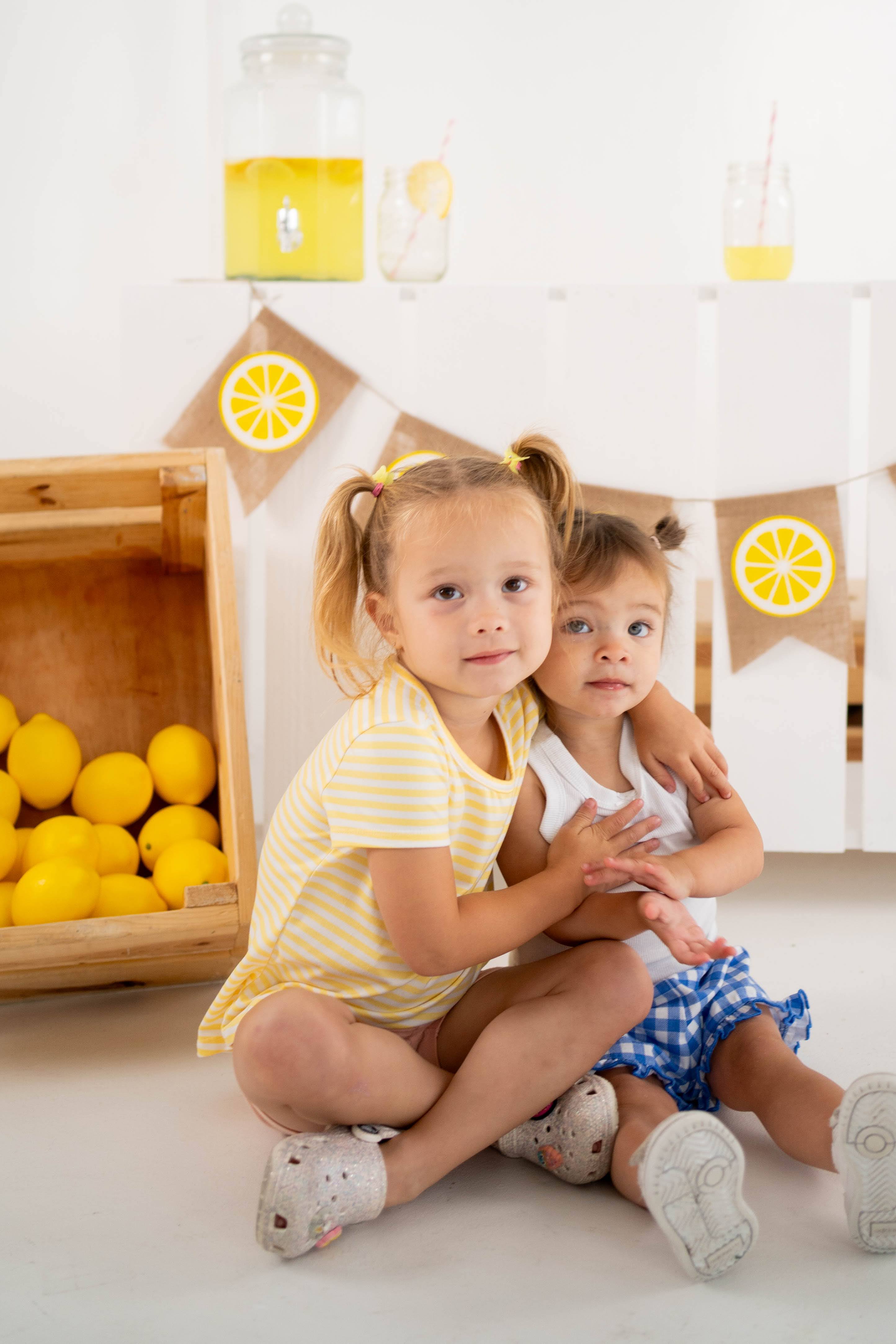 Two young sisters hugging in front of the lemonade mini stand.