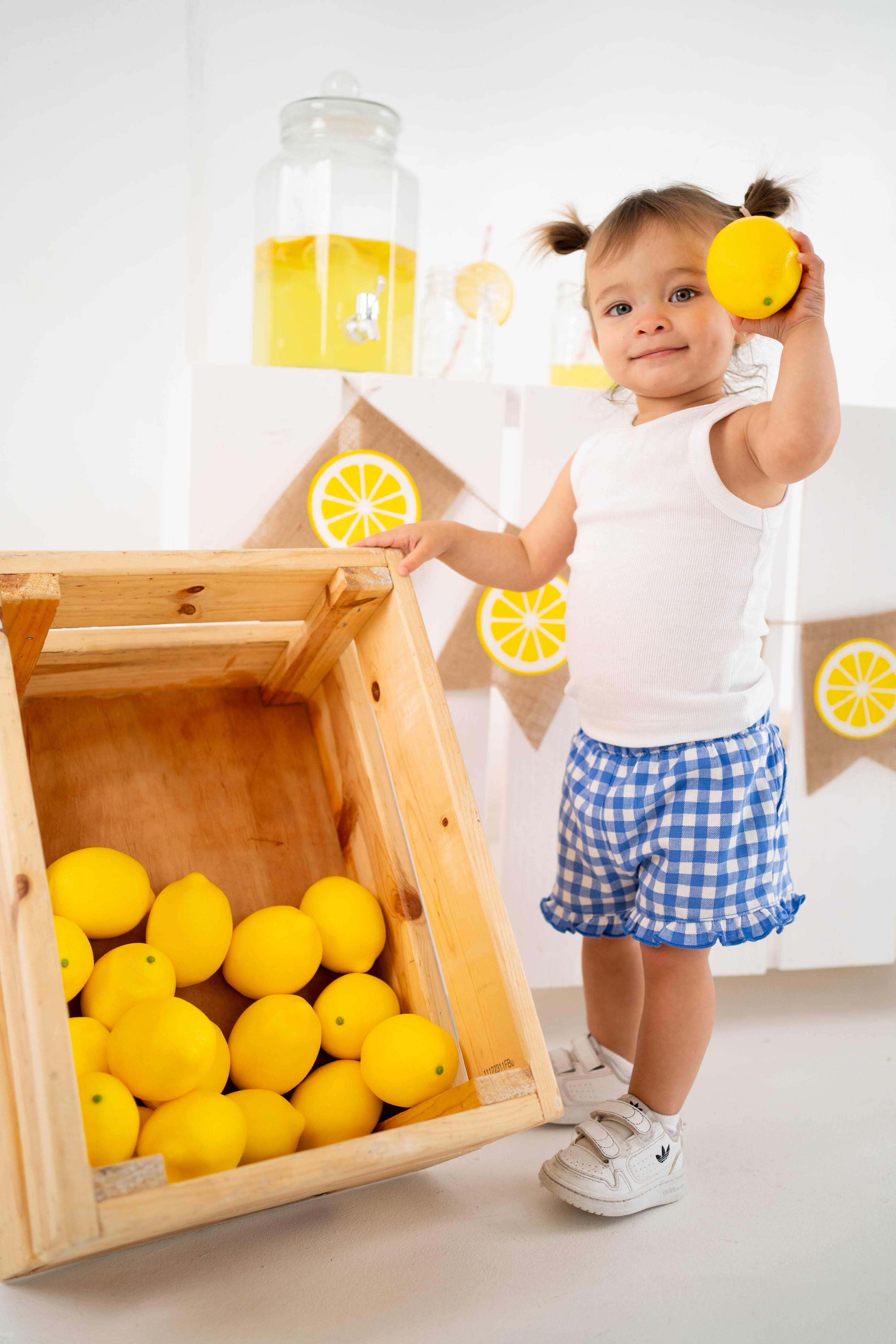 Toddler holding a lemon beside a crate of lemons.
